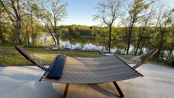 A hammock set up on a concrete surface with a view of a lake and trees.
