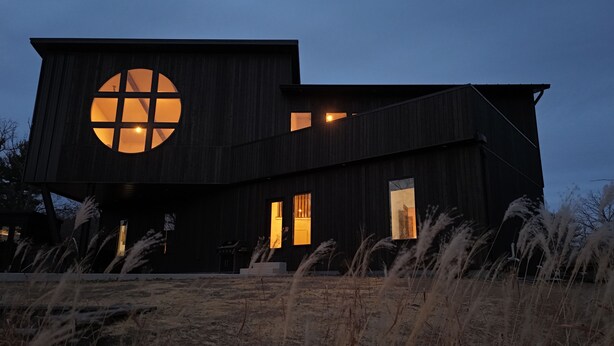 A modern two-story house with a large circular window on the left side, a smaller window on the right, and a door in the center. - The Overhang · Luxury River Retreat with Sauna, Hot Tub, Movie Theater, & Arcade (Janesville)