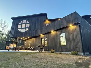 Uma casa moderna de dois andares com uma grande janela circular no andar superior, varanda coberta com assentos e área de churrasco ao ar livre.