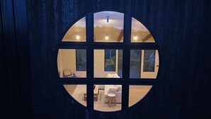A room with a large circular window, a wooden floor, a sofa, a small table, and a chair. - The Overhang · Luxury River Retreat with Sauna, Hot Tub, Movie Theater, & Arcade (Janesville)