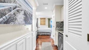 Un pasillo estrecho con una cama, una zona de cocina y un cuadro grande en la pared.