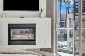 Un soggiorno moderno con camino, televisione a schermo piatto e un balcone con vista su palme e edifici.