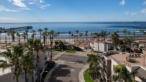 A coastal resort with a view of the ocean, palm trees, and a pier. - Relaxed Coastal Vibes - Luxury Accomodations & Steps to the Sand, Shops and Pier (Oceanside)