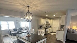 A spacious living area with a dark wood dining table, white chairs, a chandelier, and a kitchen in the background. - Escape to "Warm Mineral Springs"a Place Where You Can Relax And Heal your body. (North Port)