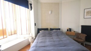 Ein Schlafzimmer mit einem großen Bett, einem Nachttisch, einem Sessel, einer Heizung und einem Fenster mit Jalousien.