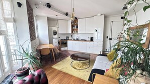 Eine moderne Küche mit weißen Schränken, ein Essbereich mit Holztisch und -stühlen sowie eine gemütliche Sitzecke mit Sofa und Couchtisch.