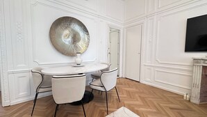 Ein Essbereich mit einem runden Tisch, zwei Stühlen, einem großen dekorativen Spiegel und einem an der Wand montierten Flachbildfernseher.