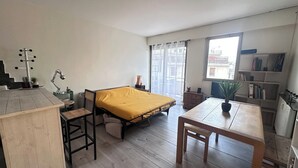 Een kleine kamer met een bed, een bureau, een stoel, een tafeltje, een boekenplank en een raam.