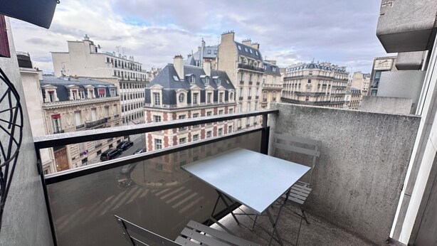 Een balkon met een tafel en stoelen, met uitzicht op een stadsgezicht met historische gebouwen.