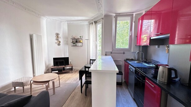 Une cuisine compacte dotée d’un îlot central, d’un coin repas avec une table ronde et d’un mur d’accent de couleur rouge.
