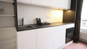 Una cocina moderna con armarios blancos, una encimera negra, un fregadero de acero inoxidable y un horno.