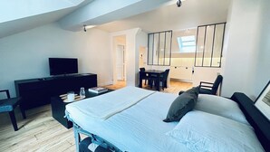 Moderni hotellihuone, jossa on sänky, työpöytä, televisio ja ruokailutila.