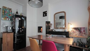 Cocina compacta con un refrigerador negro, una mesa de madera y dos sillas. Hay un espejo sobre el lavamanos y una repisa con botellas y frascos.