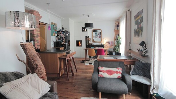 Una sala de estar moderna con piso de madera, un sillón gris, un sofá y un comedor con mesa y sillas.