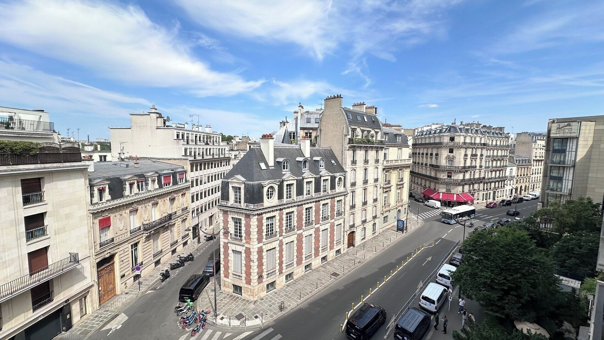 Um edifício histórico com arquitetura clássica, vista da rua com carros e um ônibus, e um céu azul límpido.