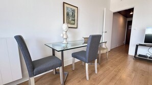 A dining area with a glass table and two grey upholstered chairs, a bust sculpture, and a framed painting on the wall. - Studio balcony and fiber – Parc Monceau 8th (Paris)