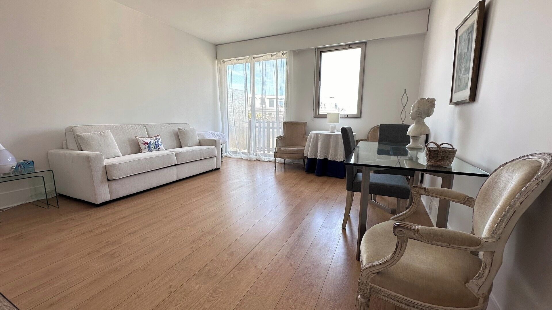 A spacious living area with a white sofa, a glass dining table, and a wooden floor.