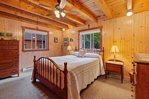 A wooden-paneled bedroom with a bed, two bedside tables, a dresser, and a ceiling fan.