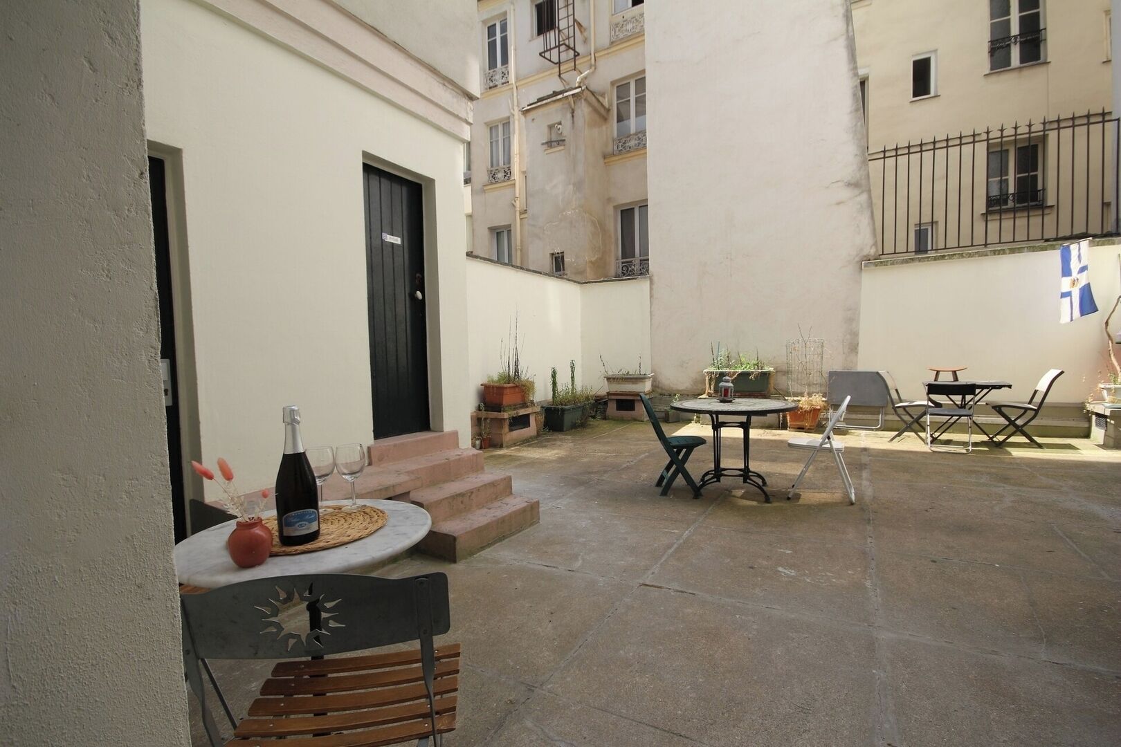 A courtyard with a table, chairs, and a bench. There is a door and a window visible.