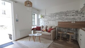 Uma sala de estar moderna com um sofá bege, duas mesinhas de cabeceira brancas e uma janela grande.