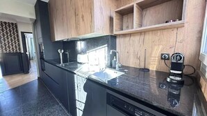 A modern kitchen with black countertops, wooden cabinets, and built-in appliances. - Luxury Apartment – 3 Bedrooms / Arc de Triomphe (Paris)
