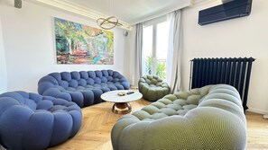 A living room with modern, tufted sofas, a round coffee table, and a large abstract painting on the wall. - Luxury Apartment – 3 Bedrooms / Arc de Triomphe (Paris)