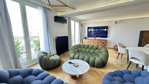 A modern living room with a large window, a flat-screen TV, and a dining area. - Luxury Apartment – 3 Bedrooms / Arc de Triomphe (Paris)