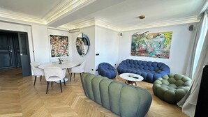 A modern living room with a dining area, a blue sofa, and green bean bag chairs. - Luxury Apartment – 3 Bedrooms / Arc de Triomphe (Paris)