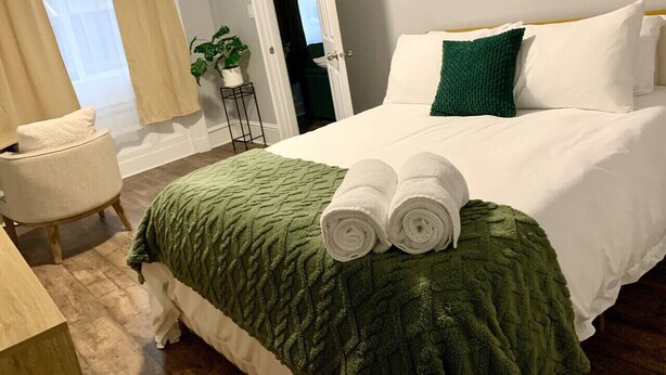 A hotel room with a bed, a chair, a plant, and a door. - Cozy 1BR by Hospital & Uptown (Saint John)