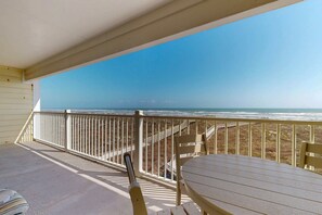 A covered outdoor area with a table and chairs, overlooking a beach with a wooden walkway. - 4002GC, Shared Pool, Great Views, Boardwalk to Beach (Port Aransas)