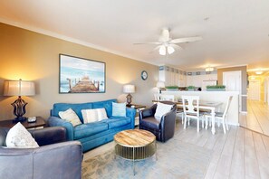 Ein Wohnzimmer mit blauem Sofa, Couchtisch und Essbereich mit weißen Stühlen und Tisch.