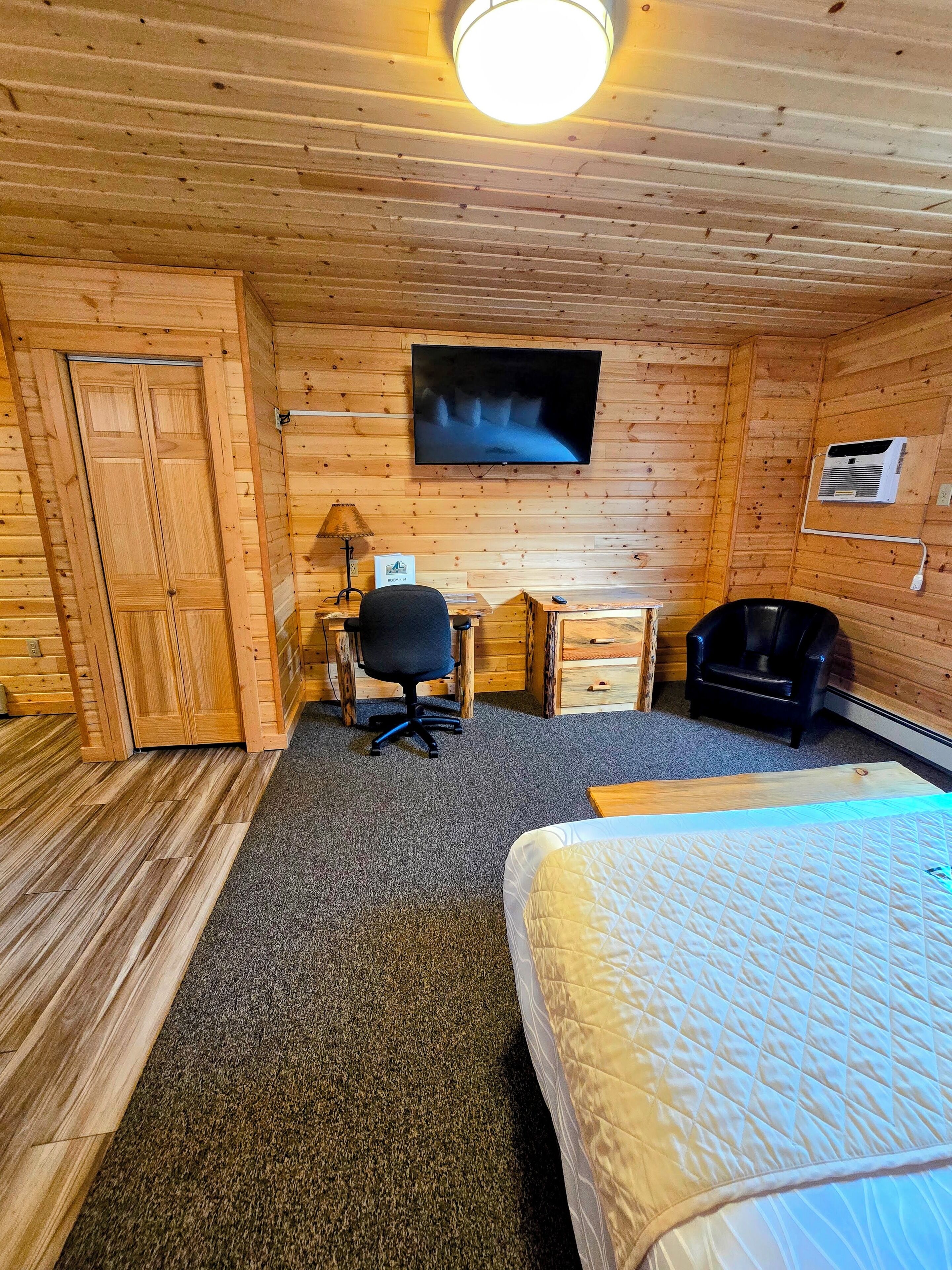 Una habitación con paneles de madera, una cama, un escritorio, una silla y un televisor.