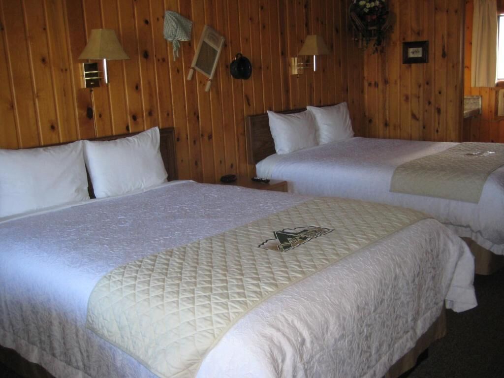 A room with two beds, wooden walls, and wall-mounted lamps.