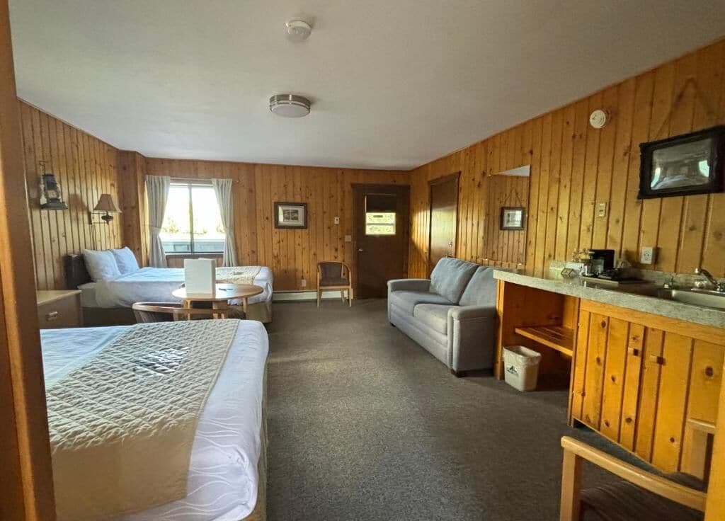 A cozy room with two beds, a sofa, a small table, and a kitchenette.