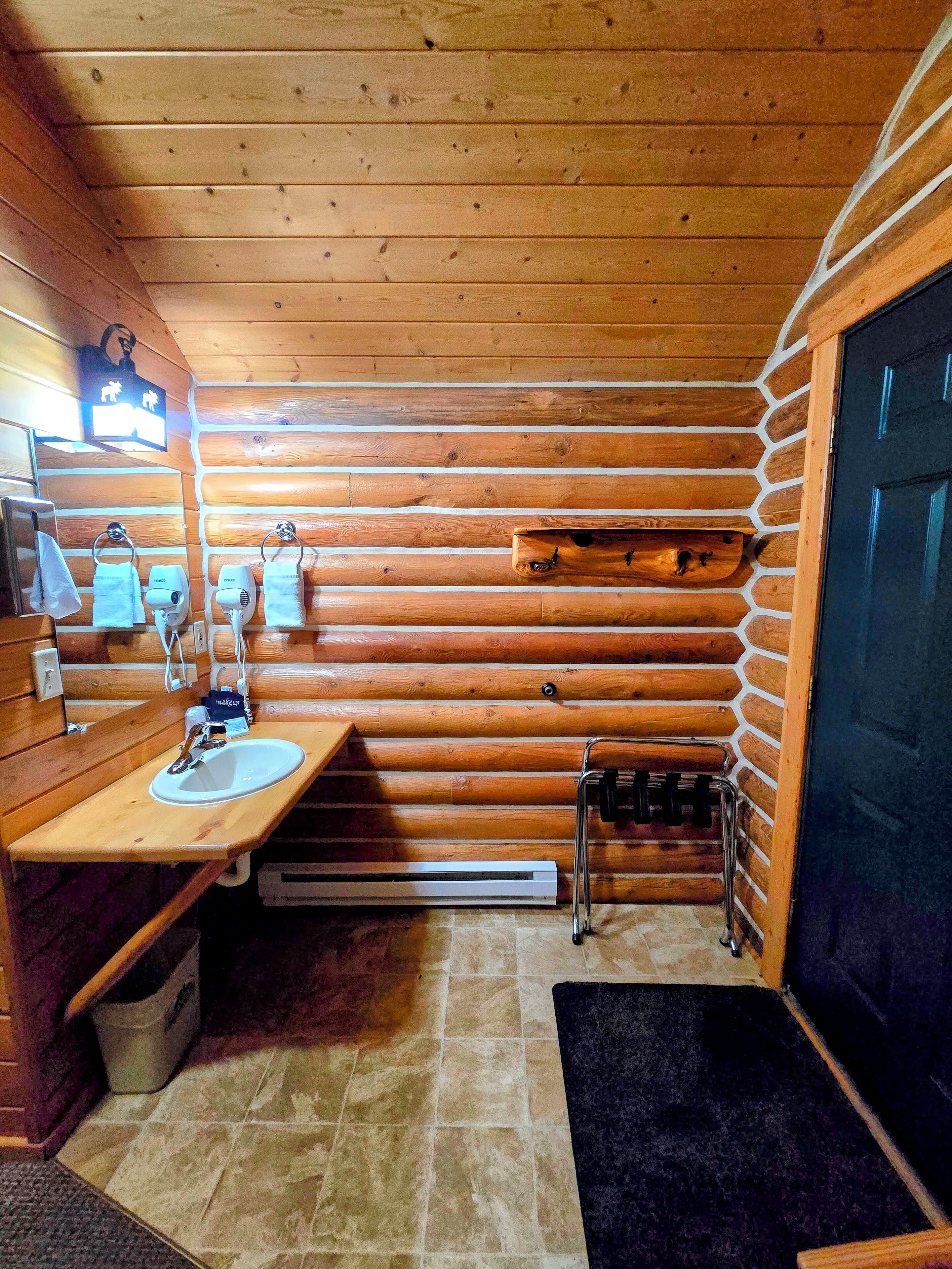 Une salle de bain rustique, aménagée dans une cabane en bois, avec un lavabo, des distributeurs de serviettes et un radiateur.