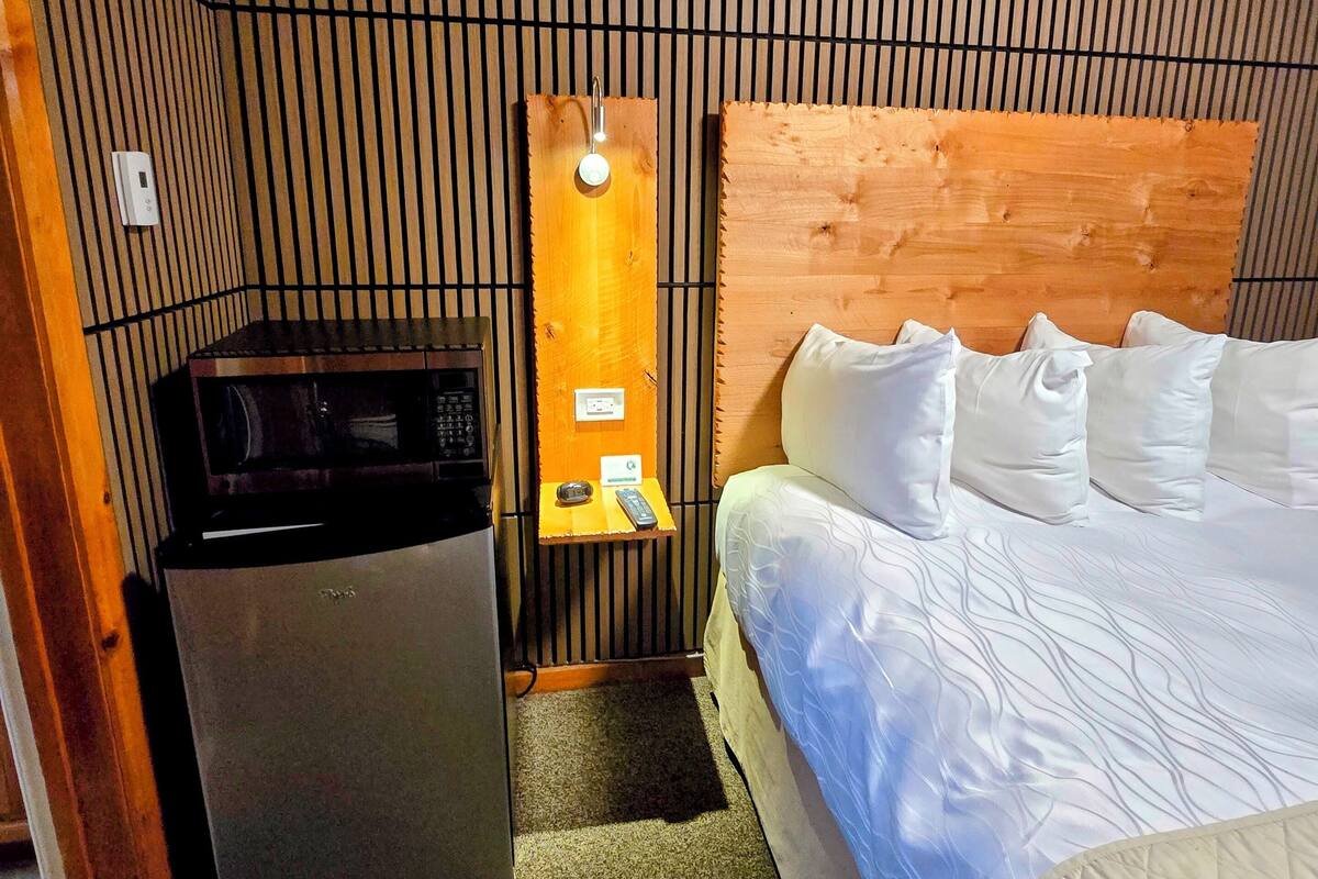 A compact room with a bed, a small refrigerator, a microwave, and a wall-mounted light fixture.