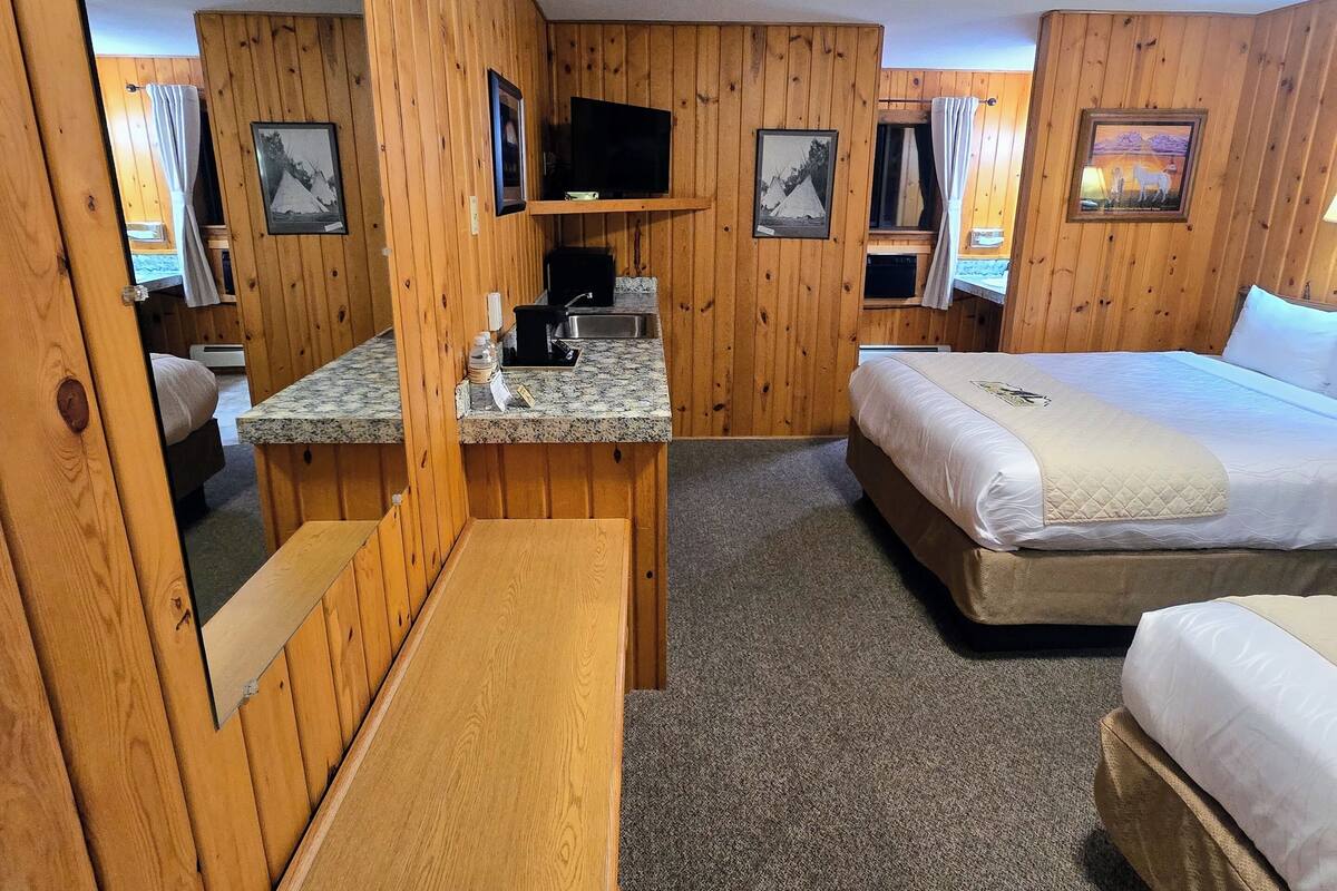A wooden-paneled room with a bed, a desk, a television, and a small kitchenette.