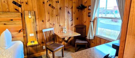A cozy cabin-style room with wooden walls, a bed, a dining table, and a small kitchen area.
