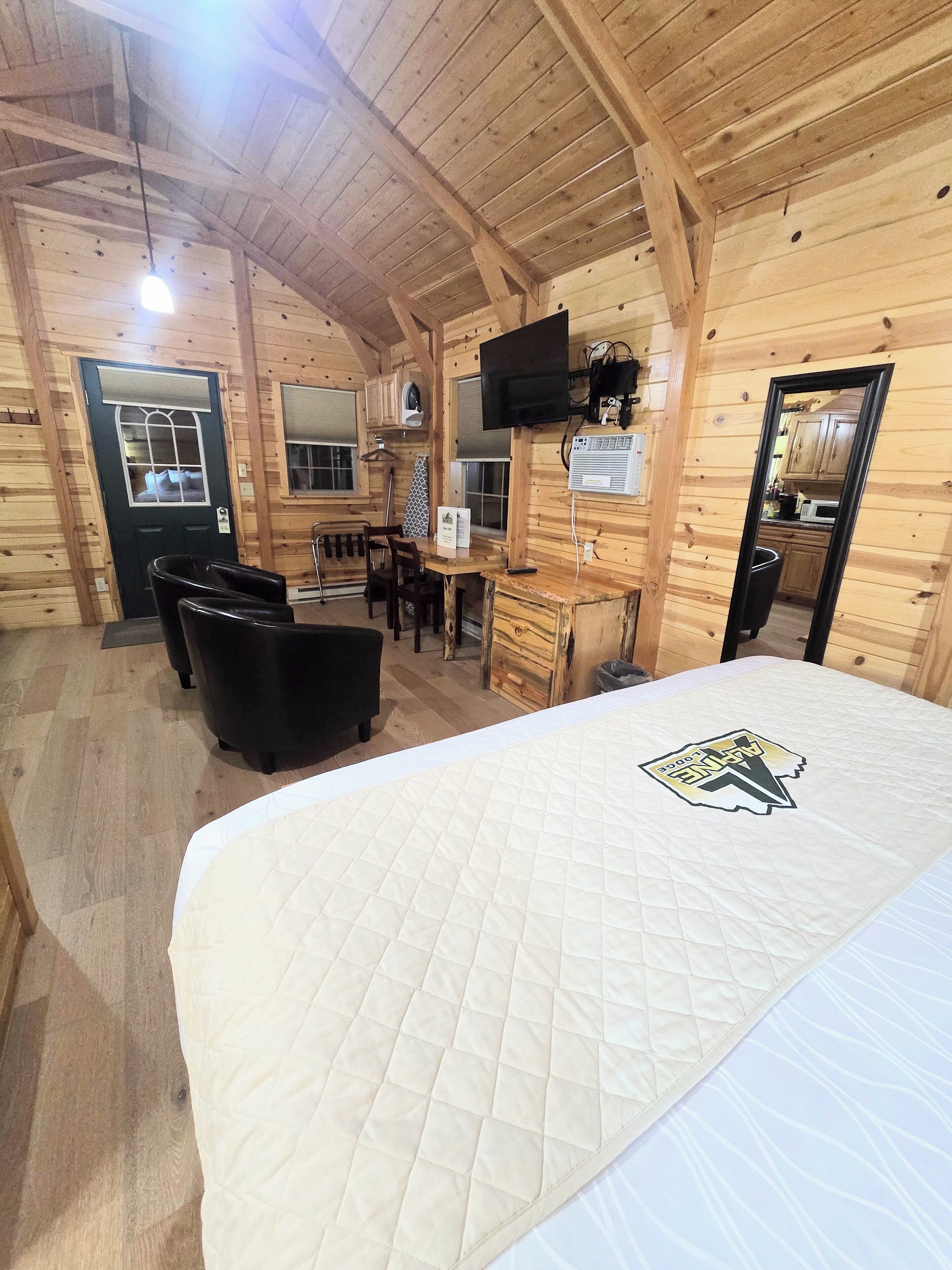 Een houten blokhut interieur met een bed, een bureau, een stoel, een televisie en een keukenhoek.