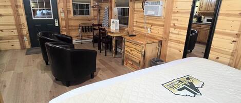 Een houten blokhut interieur met een bed, een bureau, een stoel, een televisie en een keukenhoek.