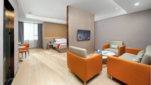 Ein Hotelzimmer mit einem Bett, zwei orangefarbenen Sessel, einer weißen Couch, einem kleinen runden Tisch und einem Bild an der Wand.