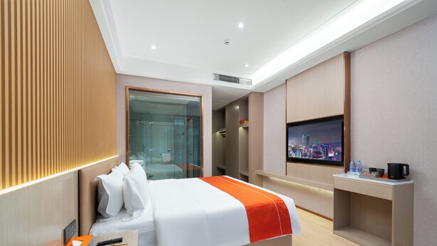 Ein modernes Hotelzimmer mit Bett, Nachttisch, Fernseher und Blick auf die Stadt.