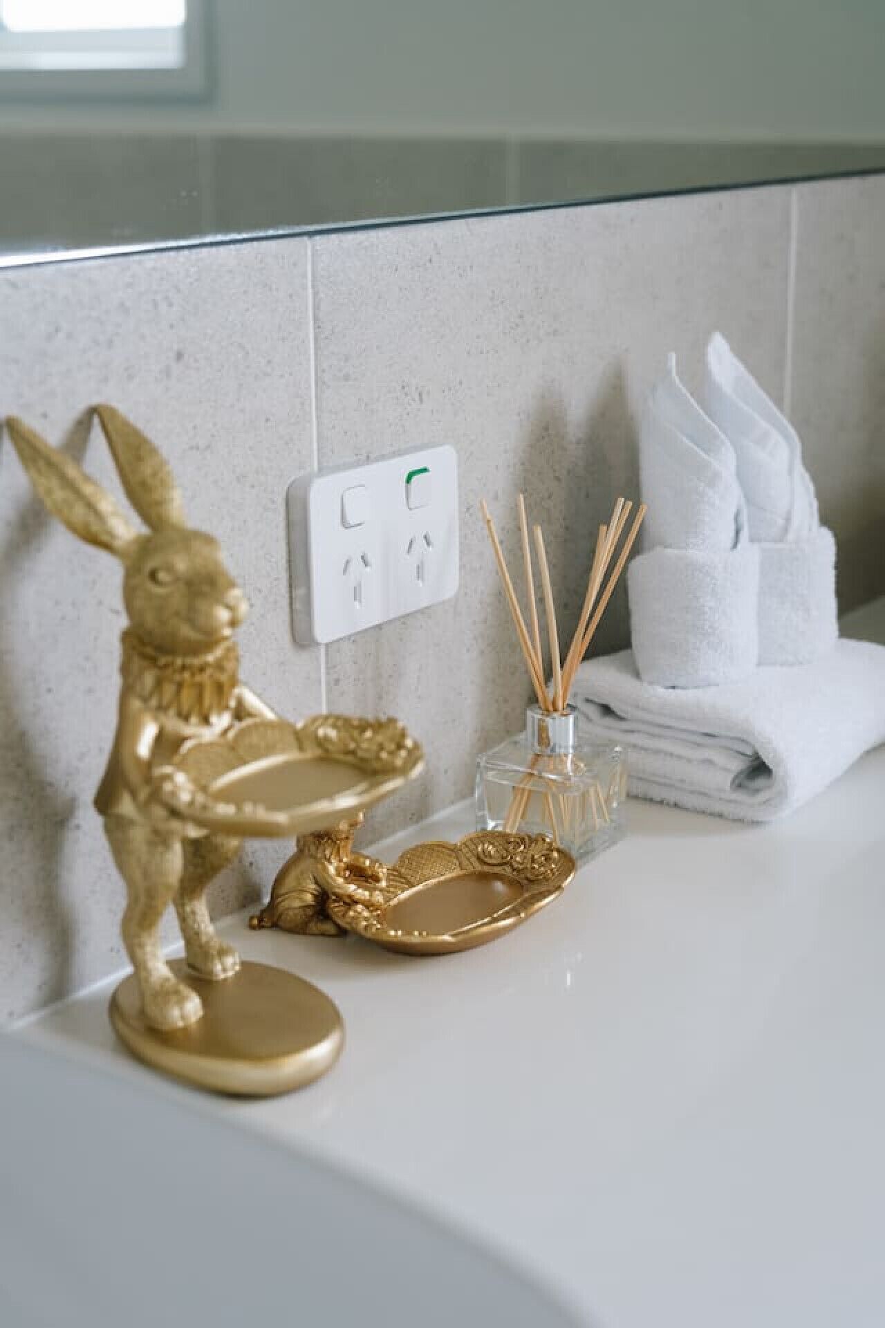 A bathroom with a gold rabbit figurine, a glass perfume bottle, and a stack of white towels on the counter.