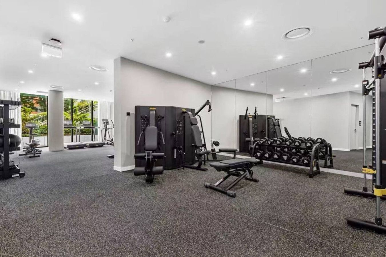Un gimnasio moderno con diversos equipos de ejercicio, incluyendo máquinas de pesas y pesas libres, y un espejo grande en la pared.