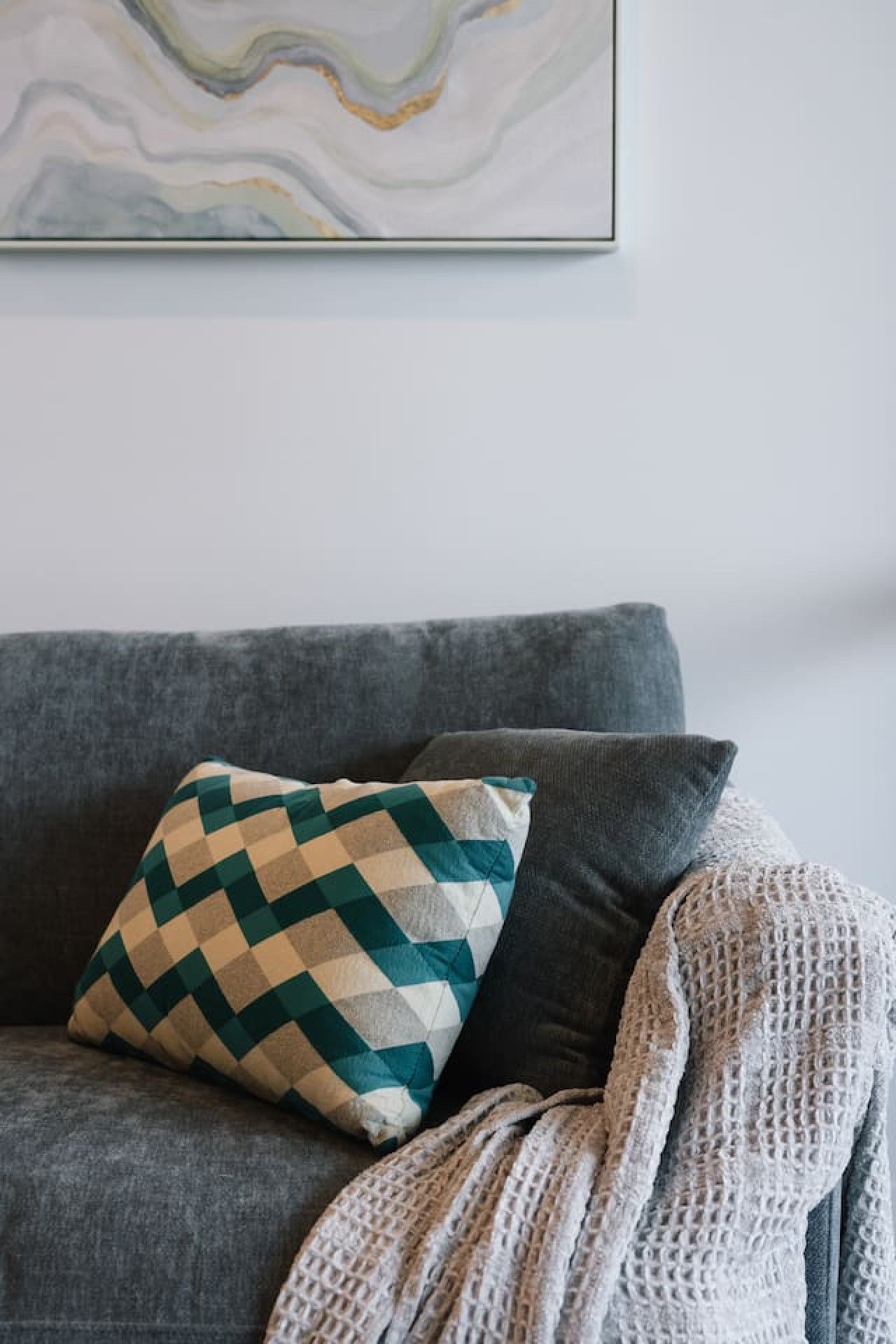 A grey sofa with a patterned pillow and a knitted throw.