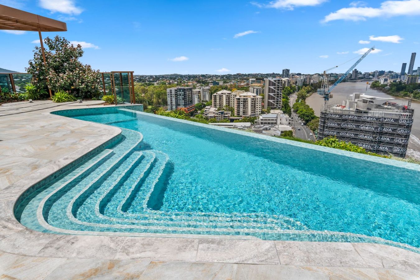 Une piscine au design incurvé, entourée d’un paysage urbain et avec une grue de construction en arrière-plan.