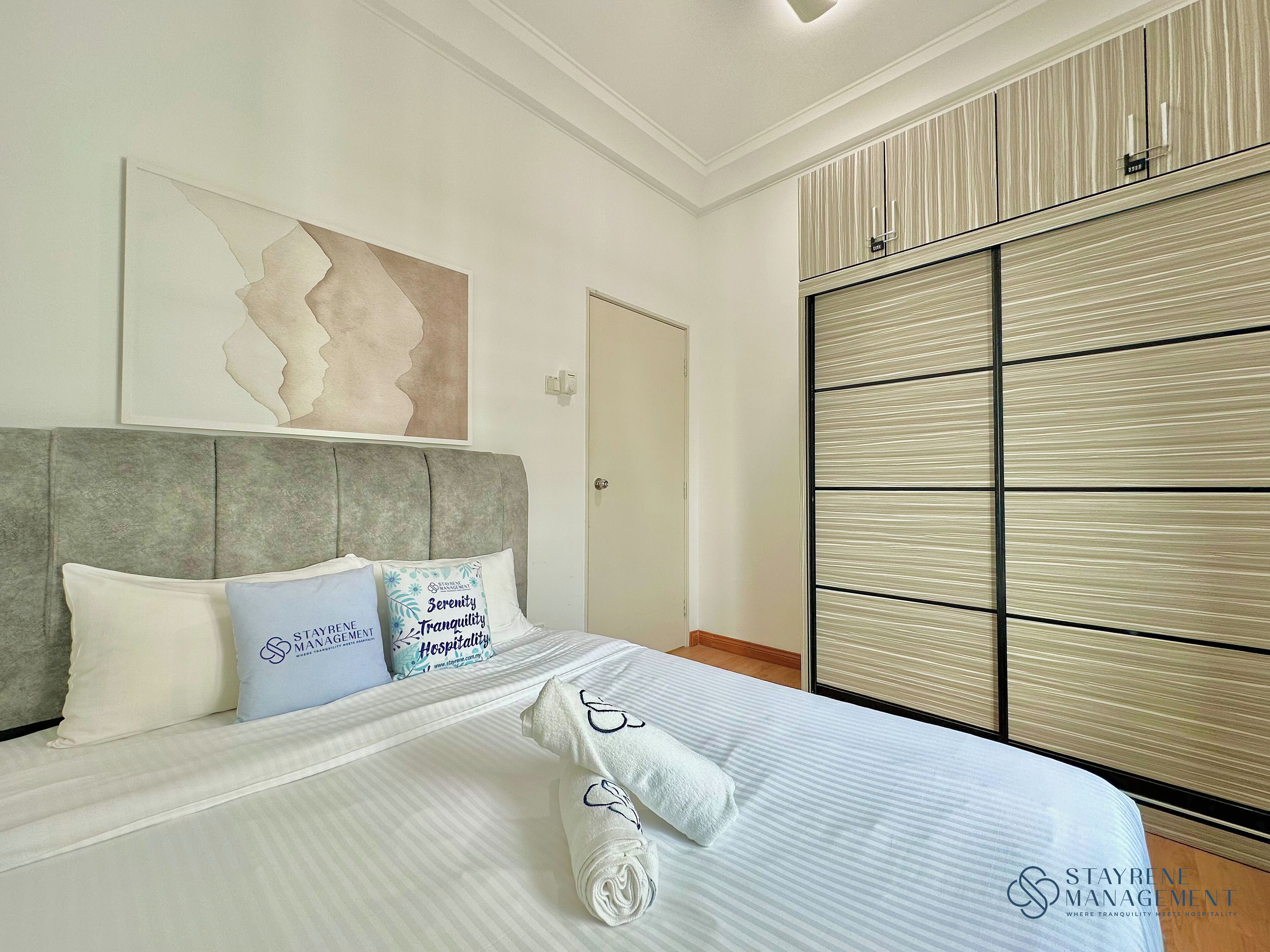 A hotel room with a bed, pillows, a headboard, a wall art piece, a door, and a wardrobe.