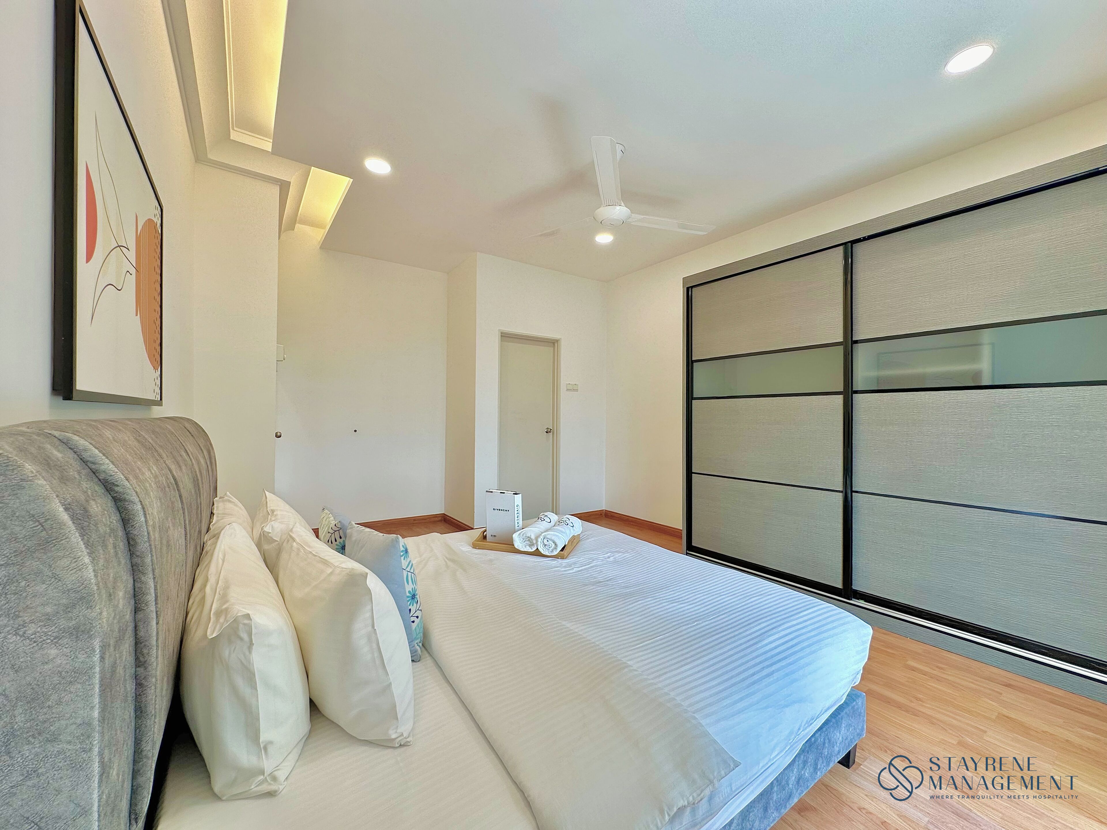A modern hotel room with a bed, pillows, a ceiling fan, and a large window with blinds.