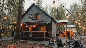 A cabin with a porch, outdoor seating, and string lights. - Alpenwolf - Sauna! Hot Tub! Firepit! EV! AC! (Ashford)