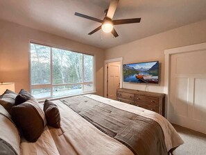 Ein Schlafzimmer mit Bett, Fernseher, Deckenventilator, Fenster und Tür.